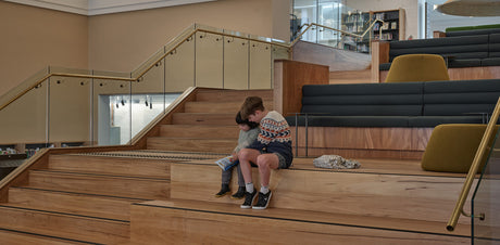 2 children sitting on accessible stairs with stair nosing, reading a book in a library.